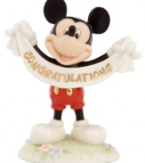 A cute memento of a major accomplishment, Mickey Mouse extends his congratulations with a gold-lettered banner in this fine china Disney figurine by Lenox.  Qualifies for Rebate