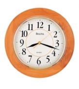 Simply classic. A timeless piece for any room, this wall clock by Bulova features a round, honey-finished wooden frame and bright gold tone bezel. White dial displays easy-to-read numerals and three hands.