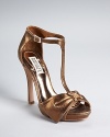 Stand tall and stately in Badgley Mischka T-strap sandals with refined jeweled bow accents, in a neutral and glamourous shade of metallic bronze.